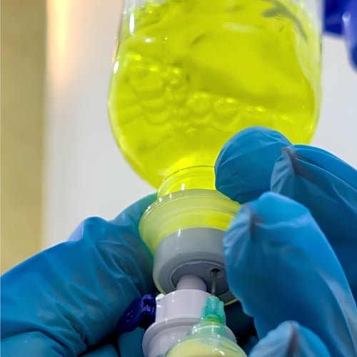 Close-up of gloved hands connecting a yellow IV bottle to its line
