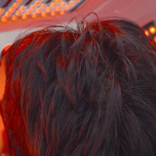 A client's hair and scalp under the warm glow of a red LED light panel